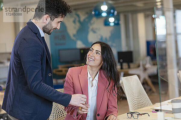 Geschäftsfrau  die lächelnd einen Stift von einem männlichen Unternehmer in einem Coworking-Büro entgegennimmt