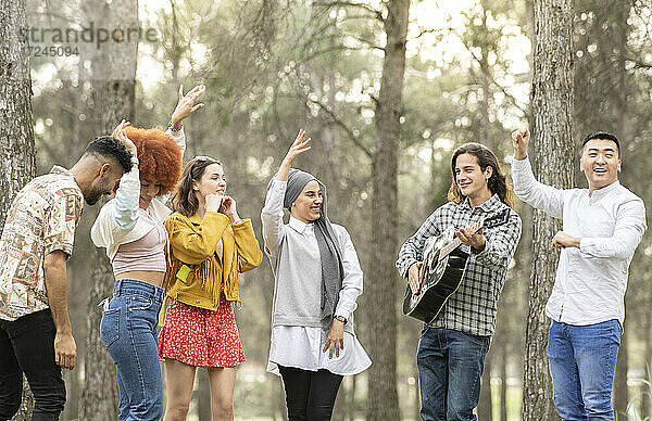 Fröhliche multiethnische weibliche und männliche Freunde tanzen und vergnügen sich im Wald