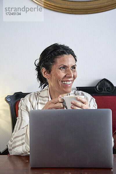 Lächelnde weibliche Fachkraft schaut weg und hält eine Kaffeetasse in einer Cafeteria