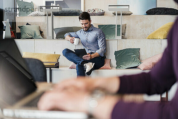 Mittlerer erwachsener Geschäftsmann mit Kaffeetasse bei der Arbeit an einem digitalen Tablet am Arbeitsplatz