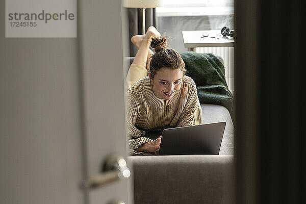 Lächelnde Frau mit Laptop auf dem Sofa zu Hause