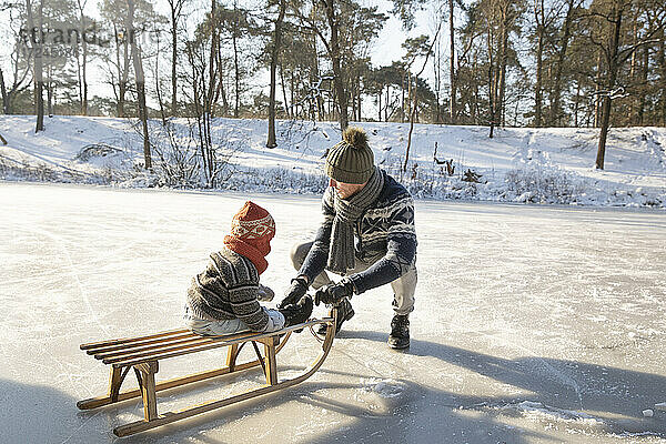 Vater bringt seinem Sohn das Schlittenfahren bei  während er im Winter im Schnee hockt