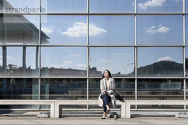 Junge Geschäftsfrau sitzt mit geschlossenen Augen auf einer Bank