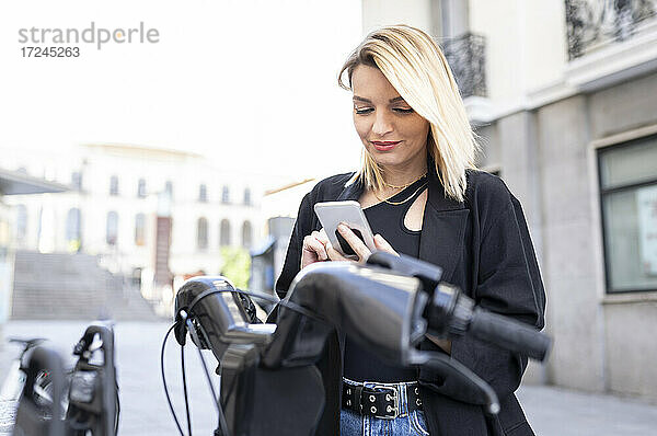 Schöne Frau mit Mobiltelefon vor einem Elektrofahrzeug