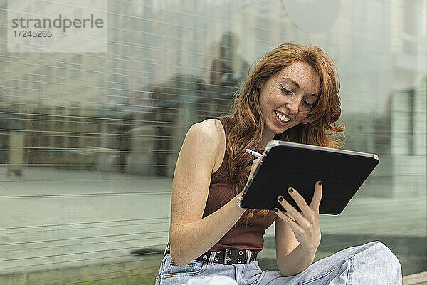 Schöne junge Frau mit digitalem Tablet vor einer Glaswand
