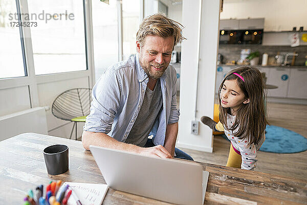 Lächelnder Vater unterrichtet seine Tochter zu Hause am Laptop