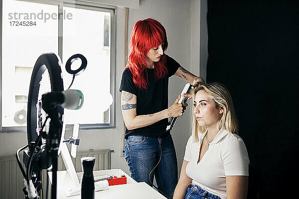 Weiblicher Friseur mit Glätteisen auf dem Haar des Modells vor Ringlicht im Studio