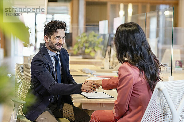 Lächelnder männlicher Unternehmer schüttelt die Hand mit einer weiblichen Fachkraft im Büro