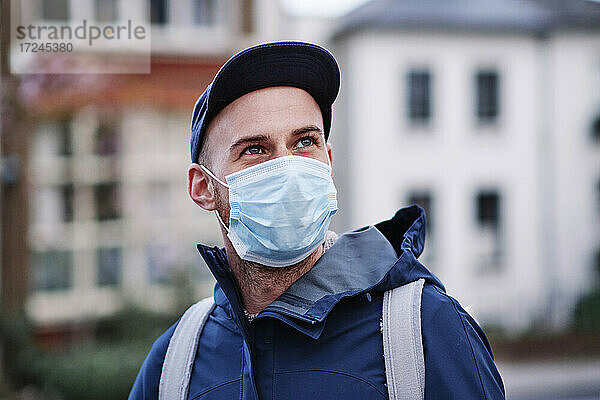 Mann mit grauen Augen  der wegschaut  während er während einer Pandemie eine Schutzmaske trägt