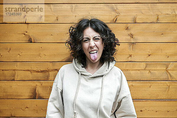 Lustige Frau  die ihre Zunge herausstreckt  während sie vor einer Holzwand steht