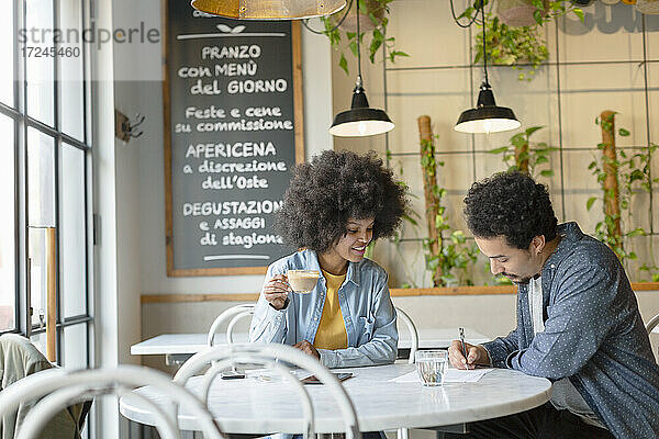 Unternehmerin betrachtet männlichen Kunden bei der Vertragsunterzeichnung in einem Cafe