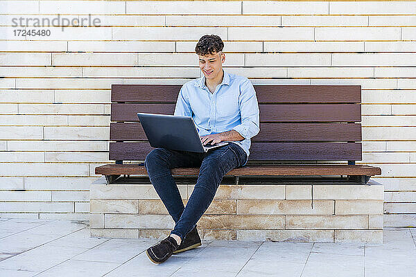 Geschäftsmann  der einen Laptop benutzt und auf einer Bank sitzt