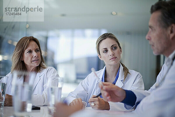 Weibliche Ärzte schauen auf einen männlichen Mitarbeiter des Gesundheitswesens  der während einer Besprechung im Krankenhaus erklärt