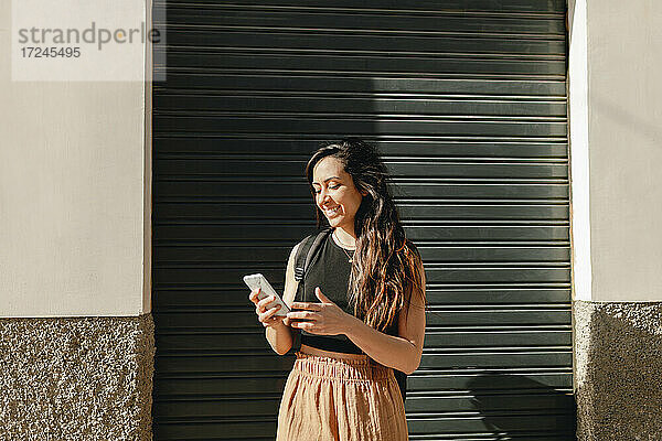 Lächelnde Touristin  die ein Smartphone benutzt  während sie vor einem Fensterladen steht