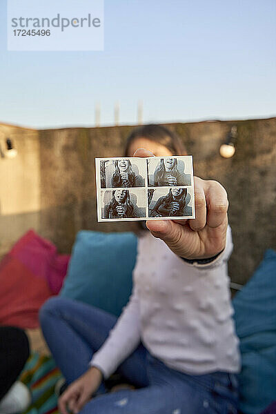 Junge Frau zeigt ein Foto  während sie auf der Terrasse eines Gebäudes sitzt