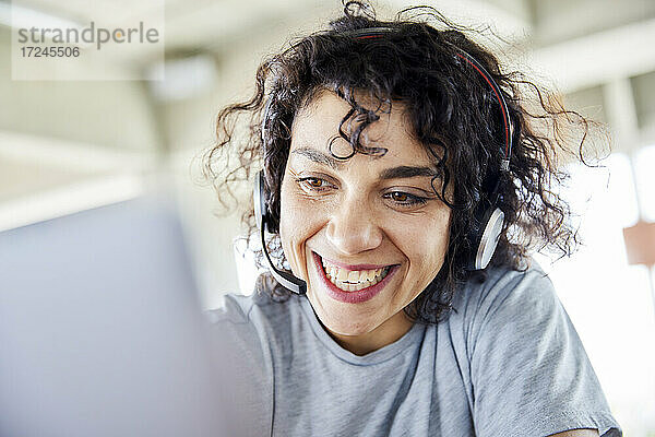 Fröhliche Frau mit Kopfhörern  die auf einen Laptop schaut