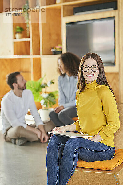 Geschäftsfrau lächelt  während sie mit Kollegen im Hintergrund in einem kreativen Büro sitzt