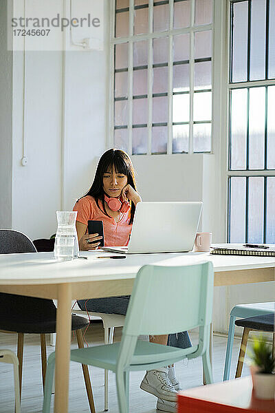 Berufstätige Frau mit Laptop und Smartphone am Tisch sitzend