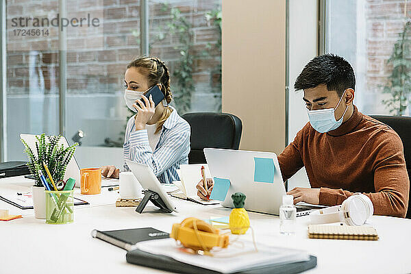 Männliche und weibliche Fachkräfte  die während COVID-19 im Büro einen Laptop benutzen