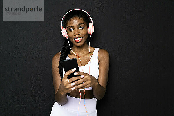Junge Frau hört Musik über Kopfhörer vor schwarzem Hintergrund