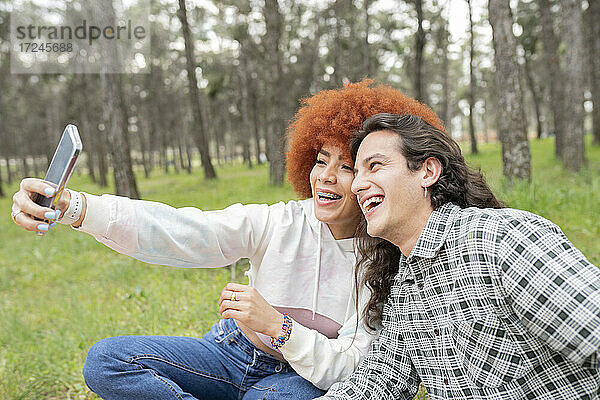 Glückliche junge Frau mit Mann nimmt Selfie durch Smartphone im Wald