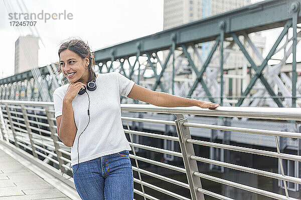Lächelnde junge Frau  die wegschaut  während sie am Geländer einer Brücke steht