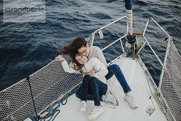Glückliche Mutter und Tochter sitzen im Urlaub auf einem Segelboot