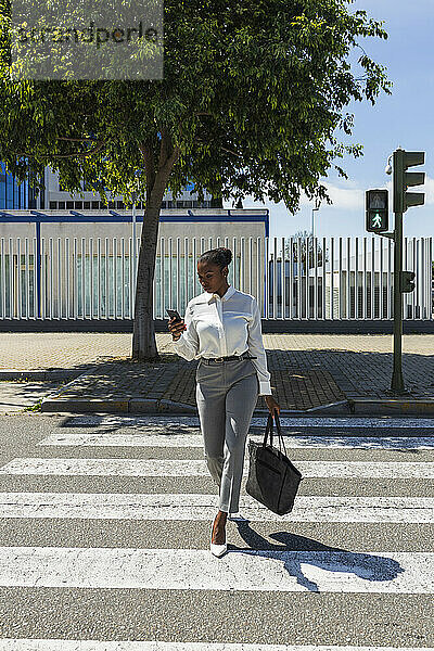 Berufstätige Frau  die ein Mobiltelefon benutzt  während sie auf der Straße geht