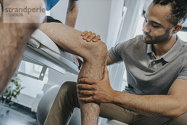 Männlicher Physiotherapeut  der das Knie eines Patienten in der Praxis untersucht