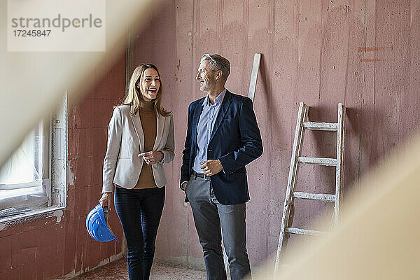 Lächelnde weibliche Kollegin im Gespräch mit einem männlichen Architekten auf der Baustelle