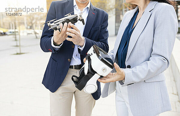 Eine Ingenieurin hält ein Virtual-Reality-Headset neben einem männlichen Kollegen mit einer Drohne im Büropark