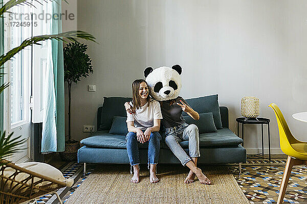 Frau mit Panda-Maske und Friedenszeichen  während sie mit ihrer Freundin zu Hause sitzt