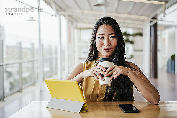 Weibliche Fachkraft hält Kaffeetasse  während sie am Tisch in der Büro-Cafeteria sitzt