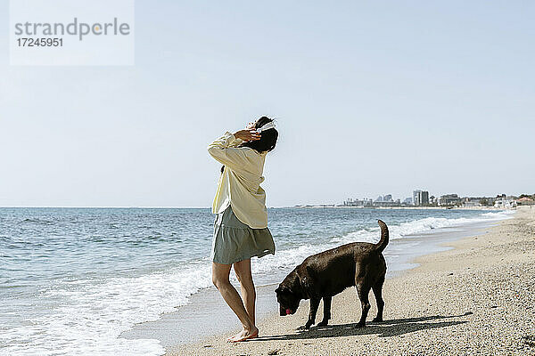 Frau hört Musik über Kopfhörer bei einem Hund am Strand
