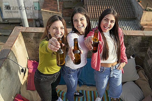 Fröhliche Freundinnen heben eine Bierflasche  während sie sich auf dem Dach vergnügen