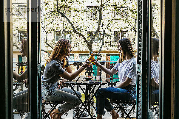 Lächelnde Freundinnen stoßen auf dem Balkon mit Bierflaschen an