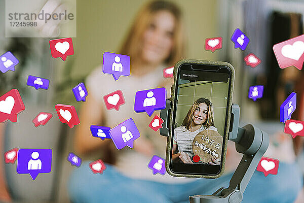 Lächelndes Teenager-Mädchen auf dem Handy-Bildschirm inmitten von Social-Media-Symbolen zu Hause