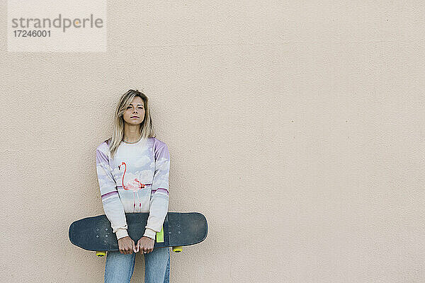 Blonde Frau mit Skateboard an der Wand lehnend