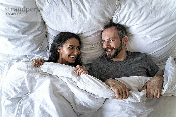 Paar  das sich gegenseitig ansieht  während es zu Hause auf einem Bett mit Decke liegt