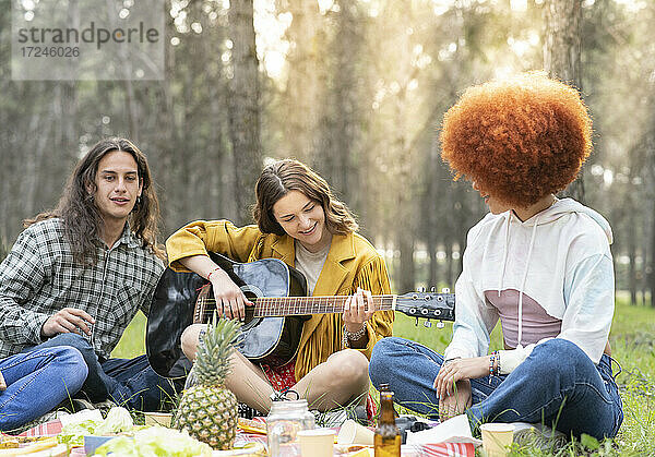 Frau mit männlichem und weiblichem Freund spielt Gitarre beim Picknick im Wald