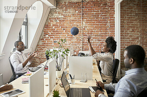 Männliche und weibliche Unternehmer spielen mit einem Ball im Coworking-Büro