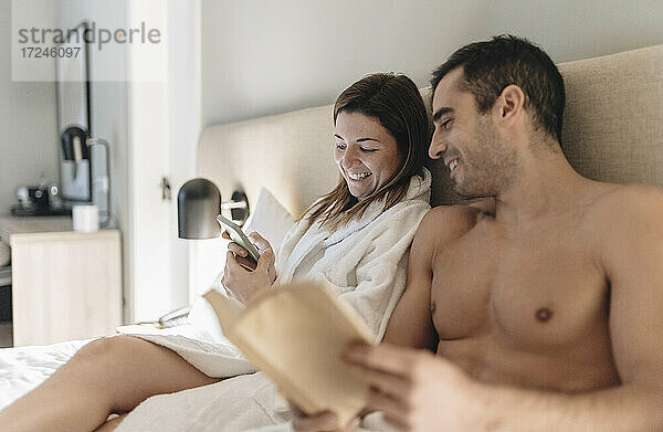 Frau benutzt Mobiltelefon  während sie neben einem Mann im Hotelzimmer sitzt