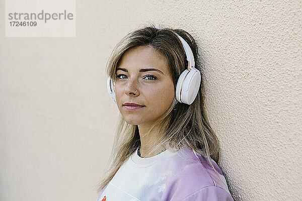 Frau mit Kopfhörern hört Musik  während sie sich an die Wand lehnt