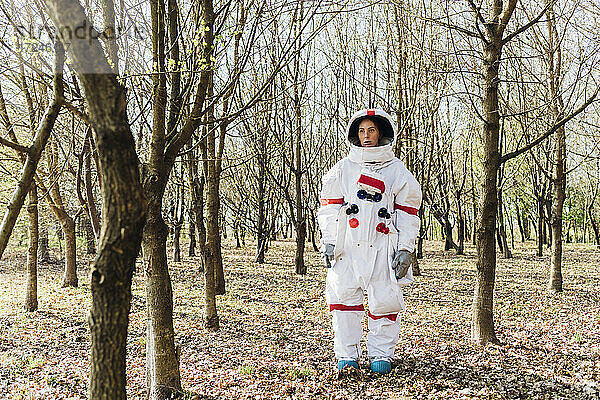 Junge Astronautin im Weltraum  die an einem kahlen Baum im Wald steht und nachdenkt