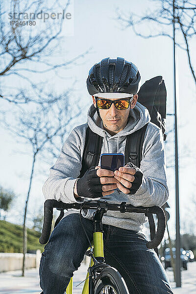 Älterer Zusteller  der sich auf ein Fahrrad stützt und ein Smartphone benutzt