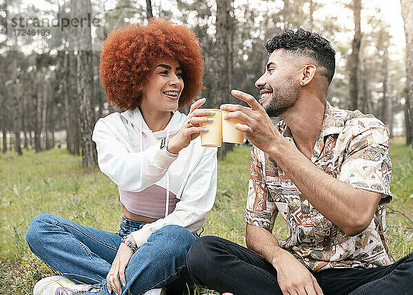 Junger Mann und schöne Frau stoßen mit Gläsern an  während sie im Wald sitzen