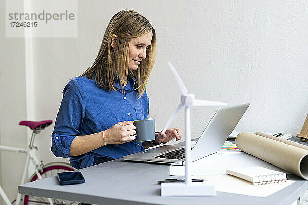 Geschäftsfrau hält Kaffeetasse und benutzt Laptop im Büro