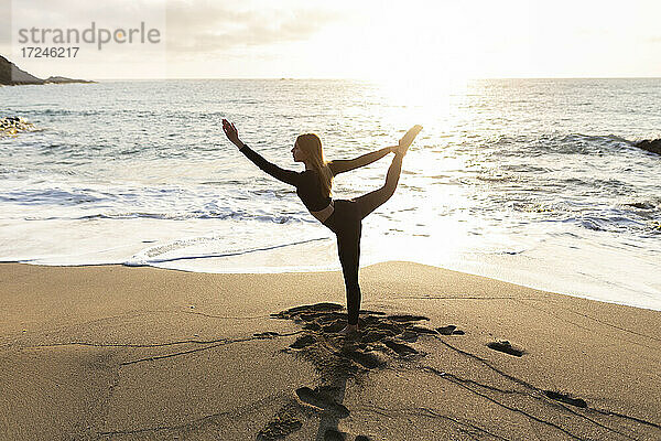 Frau dehnt sich beim Yoga am Strand am Rande des Wassers