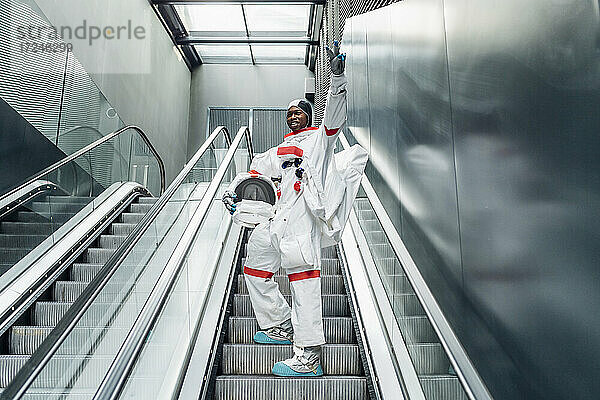 Fröhlicher Astronaut  der beim Besteigen einer Rolltreppe das Friedenszeichen macht
