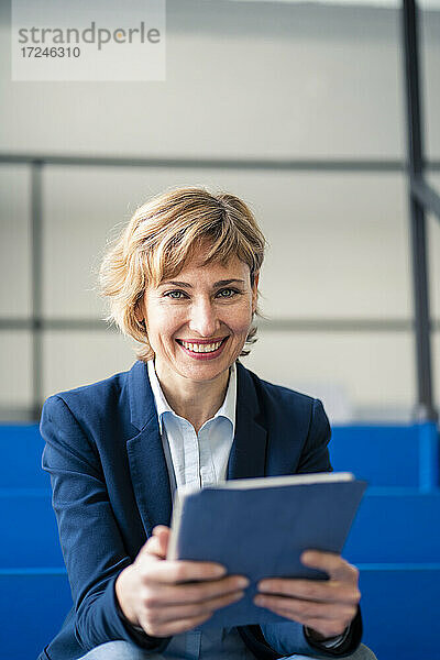 Lächelnde weibliche Fachkraft mit digitalem Tablet in der Industrie sitzend
